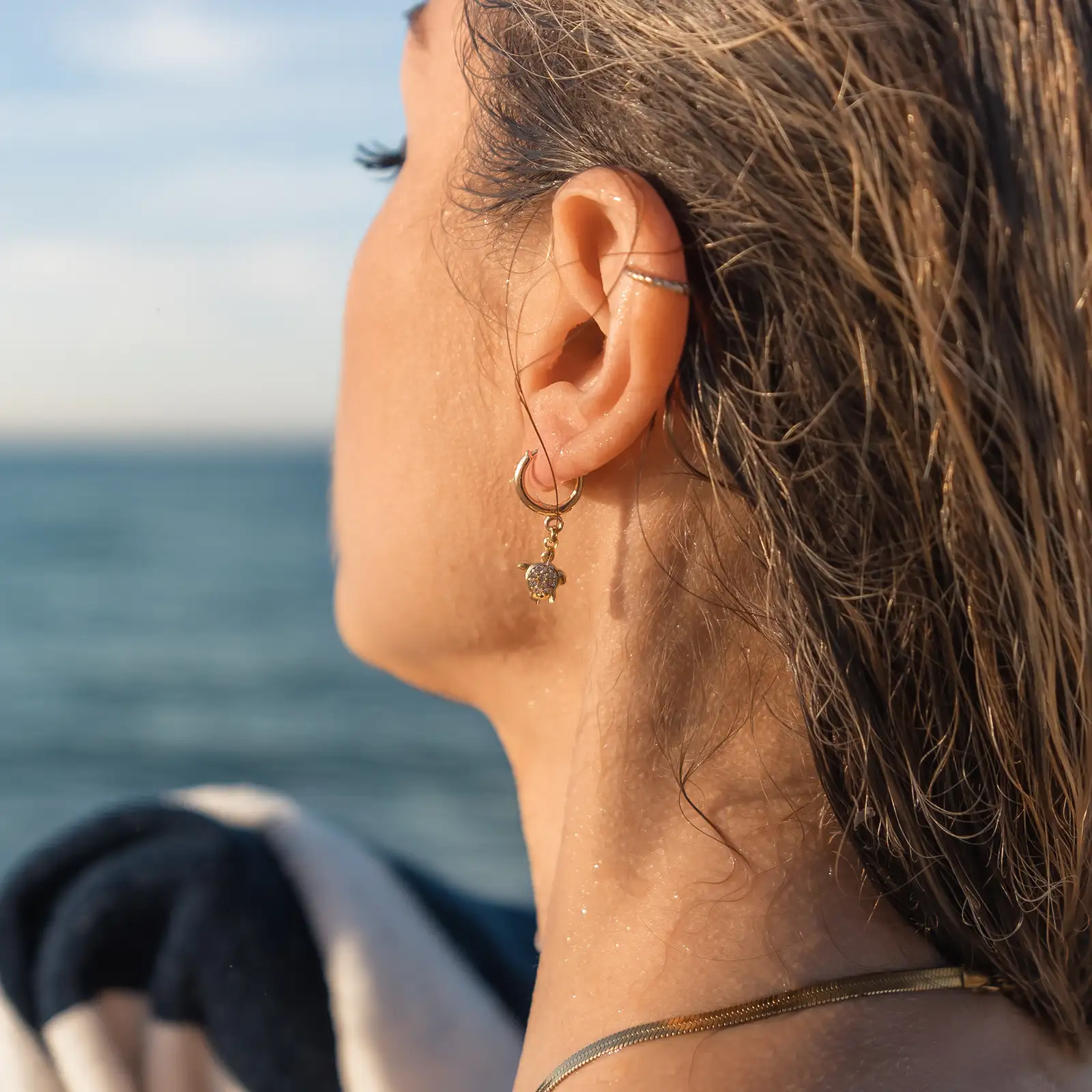 Une femme porte une boucle d'oreille ornée de son pendentif tortue. Un bijou DENADDA