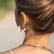 Une femme porte une boucle d'oreille créole en perle de pierre de lave blanche. Etna un bijou fait main par DENADDA.