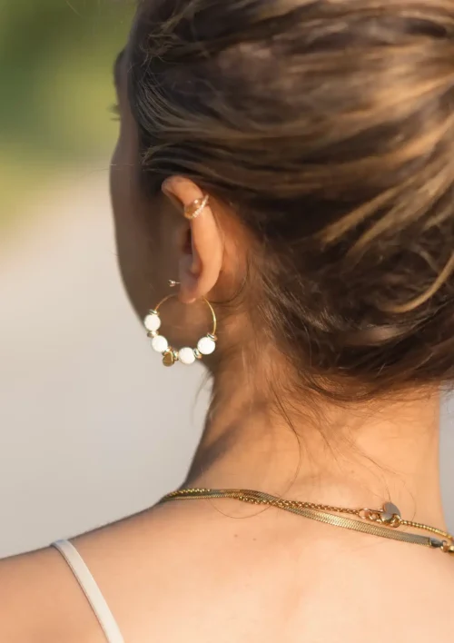 Boucle d'oreille créole pierre de lave blanche - Etna Une femme porte une boucle d'oreille créole en perle de pierre de lave blanche. Etna un bijou fait main par DENADDA.