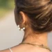 Une femme porte une boucle d'oreille créole en perle de pierre de lave blanche. Etna un bijou fait main par DENADDA.