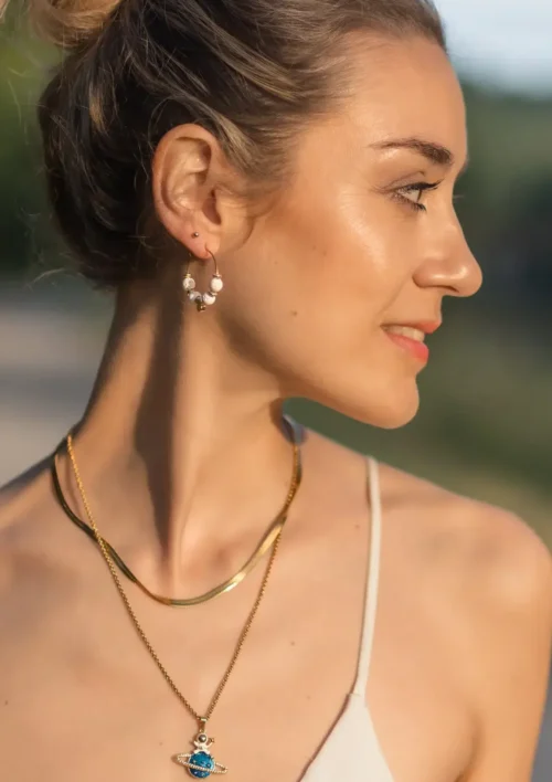 Boucle d'oreille créole pierre de lave blanche - Etna Une femme porte une boucle d'oreille en perle de pierre de lave blanche. Un bijou élégant fait main par DENADDA.