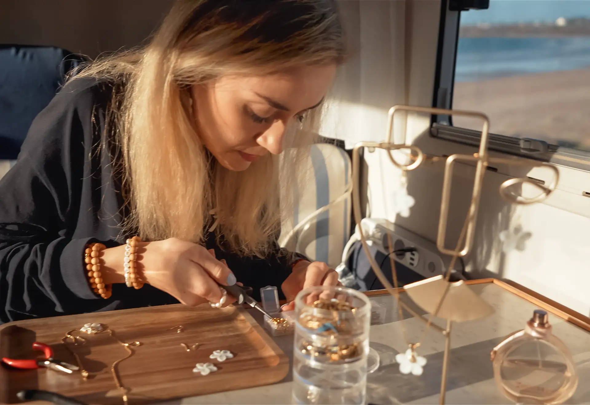 Elma confectionne des bijoux faits main au bord de la mer dans son atelier de création roulant DENADDA.