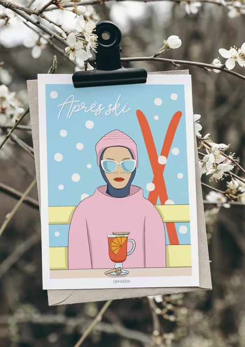 Affiche après-ski minimaliste "Bleu et rose sous la neige" Affiche après-ski minimaliste bleu et rose sous la neige – illustration Playful Denadda suspendue à une branche fleurie en extérieur en hiver, ambiance naturelle et poétique.
