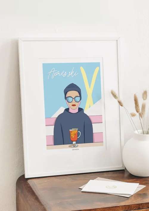 Cadre après-ski minimaliste "Bleu et jaune" Cadre après-ski minimaliste bleu et jaune – Collection Playful Denadda en mise en situation déco intérieure, posée sur un meuble en bois avec vase blanc.