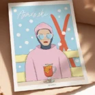 Poster ski minimaliste Après-ski bleu et rose sous la neige – illustration Playful Denadda photographiée en mise en situation déco, posée sur une surface beige avec lumière naturelle.