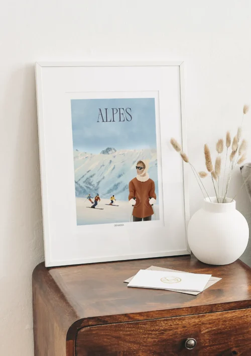 Cadre Alpes "Ski vintage" Cadre Alpes ski vintage posé sur un meuble, illustration artistique Denadda avec skieurs en descente et personnage en premier plan.