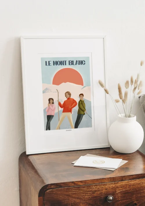 Cadre Mont Blanc vintage Cadre Mont Blanc vintage signé Denadda, posé sur un meuble en bois, avec illustration rétro de skieurs devant le massif et un grand soleil orangé.
